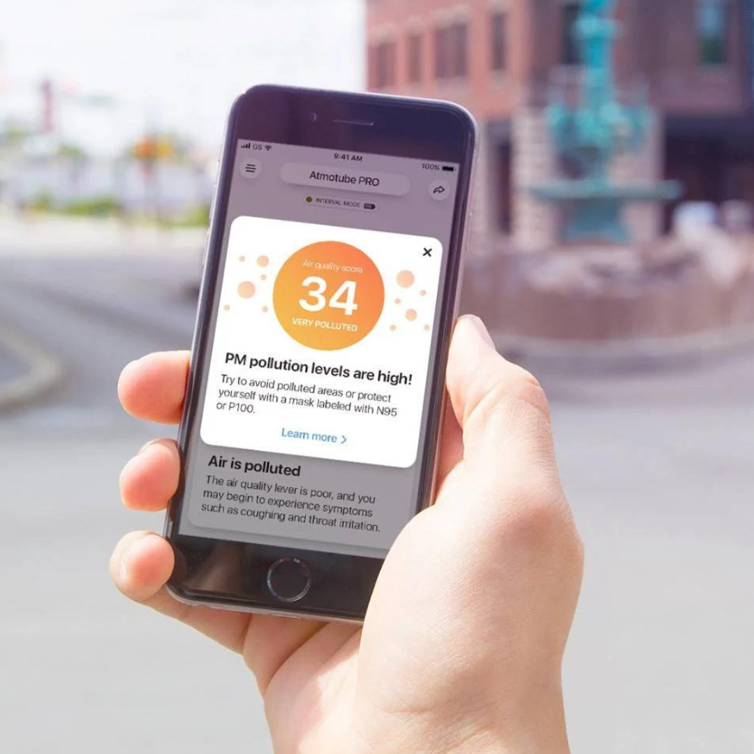 A person is holding a smartphone with an app displaying an air quality score and pollution alert.