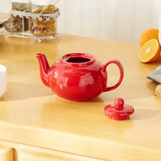 Red ceramic teapot with lid off, on a wooden surface.