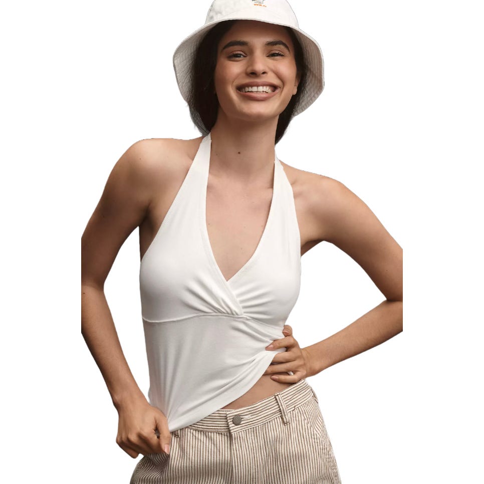 A smiling person wearing a white halter top paired with high-waisted striped pants and a white bucket hat.