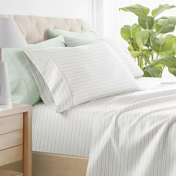 Striped bedding set on a bed, including pillows, sheets, and a comforter, in a room with a plant and a nightstand.