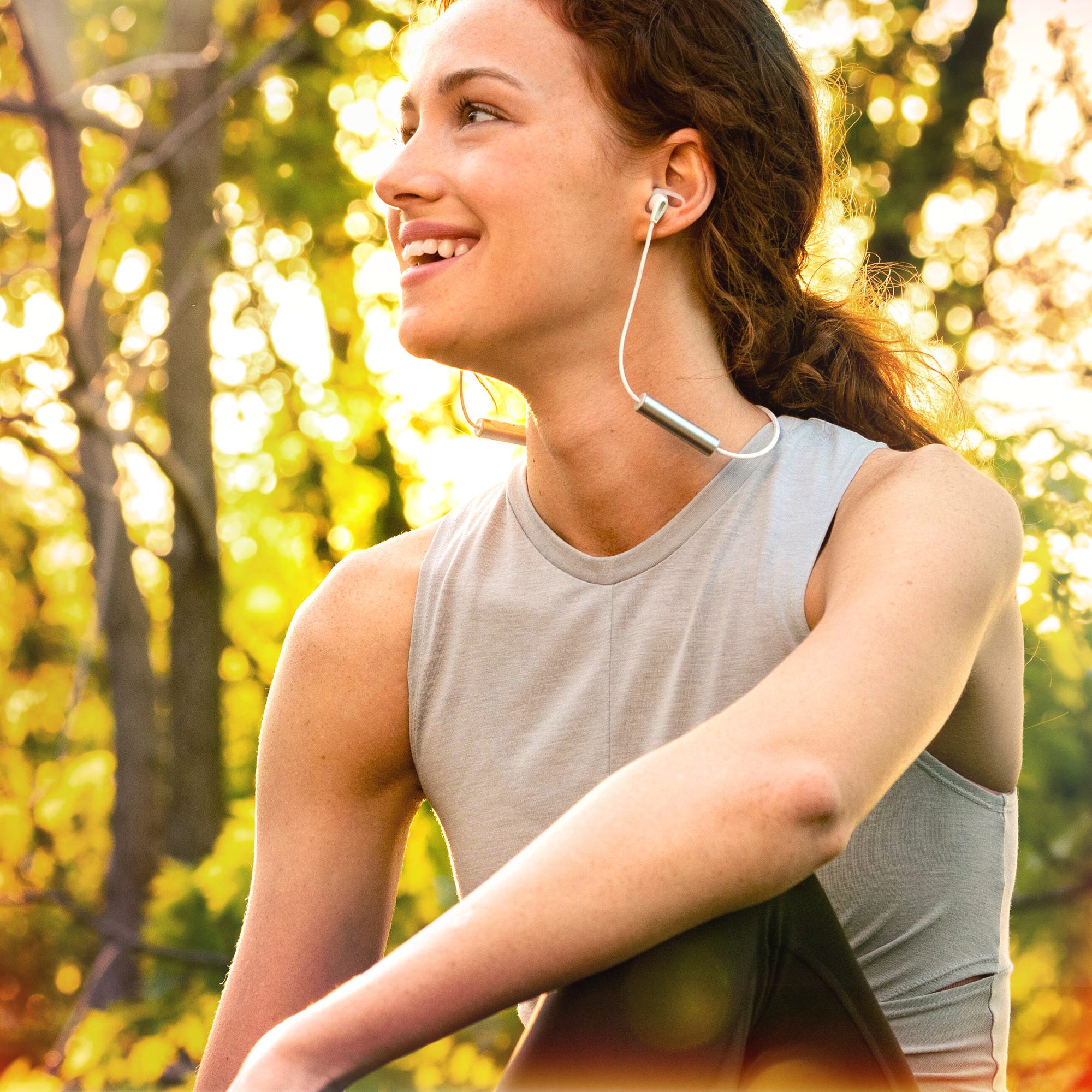 A woman wearing wired earphones and a sleeveless top outdoors.