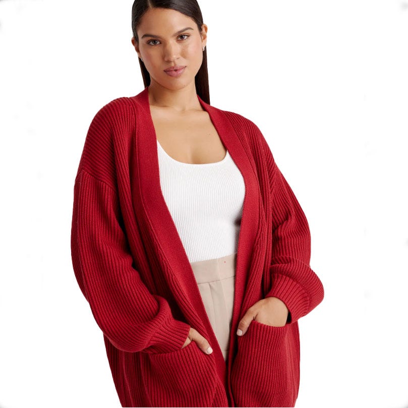 A woman wears a deep red, oversized, ribbed cotton cardigan with drop shoulders, long sleeves, and front pockets over a white tank top.