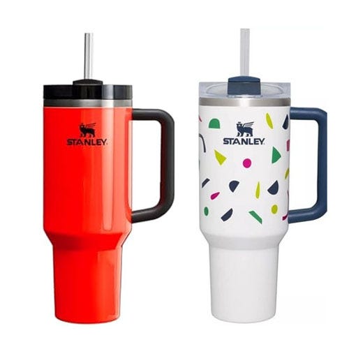 Two Stanley insulated travel mugs with straws, one red and one white with colorful confetti pattern.