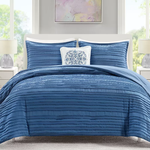 A blue quilted comforter set on a bed, with matching pillows and one decorative white pillow with a blue pattern.