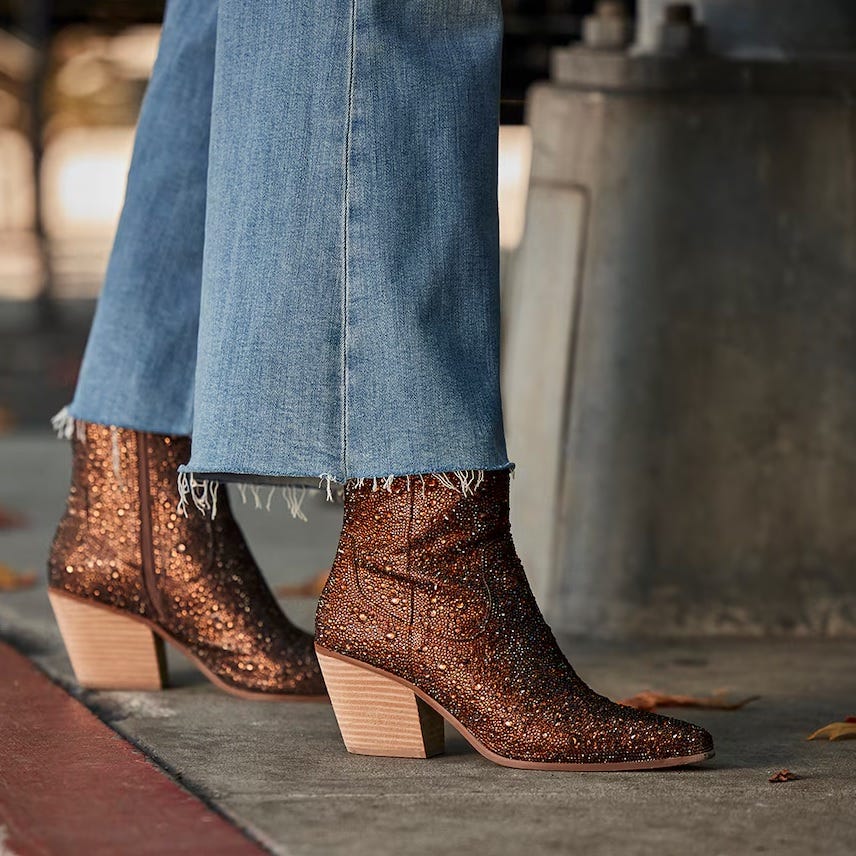 A pair of glittery brown ankle boots with chunky heels, paired with frayed hem blue denim jeans.