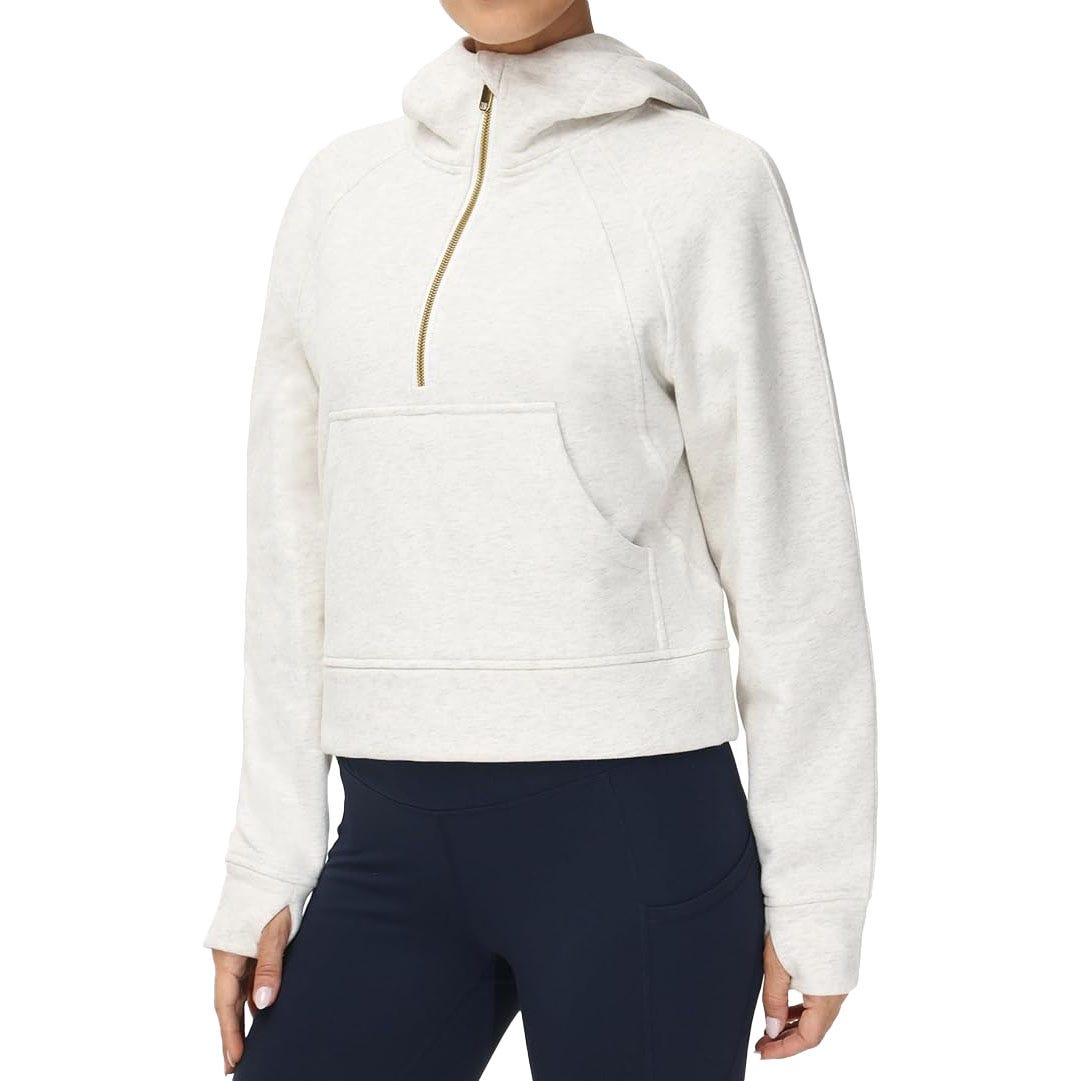 Off-white hooded pullover with a gold half-zip, kangaroo pocket, and long sleeves, paired with navy leggings.
