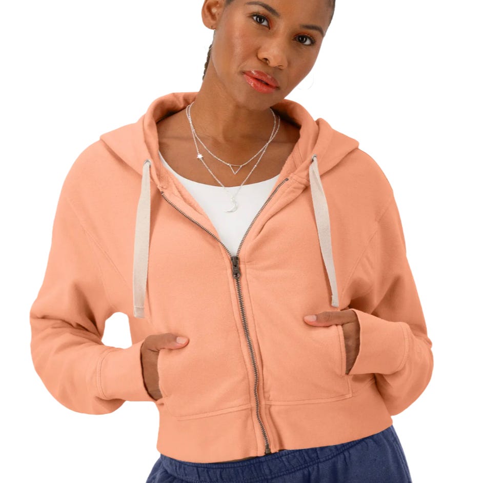 A peach-colored Champion zip hoodie with a drawstring hood and front pockets, worn by a woman.