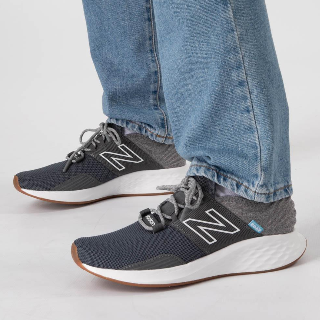 A pair of dark gray athletic shoes with a prominent 'N' logo, worn with light blue jeans.