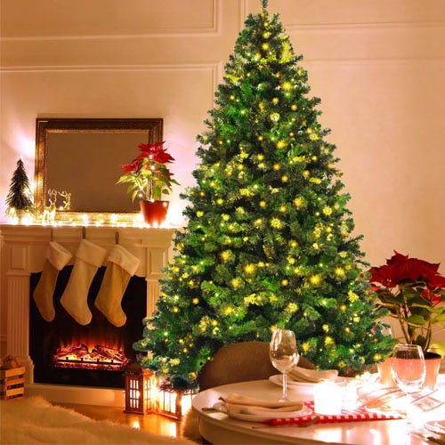 A decorated Christmas tree stands beside a fireplace adorned with stockings and a poinsettia plant. The room is warmly lit, and a dining table is set with candles and wine glasses.