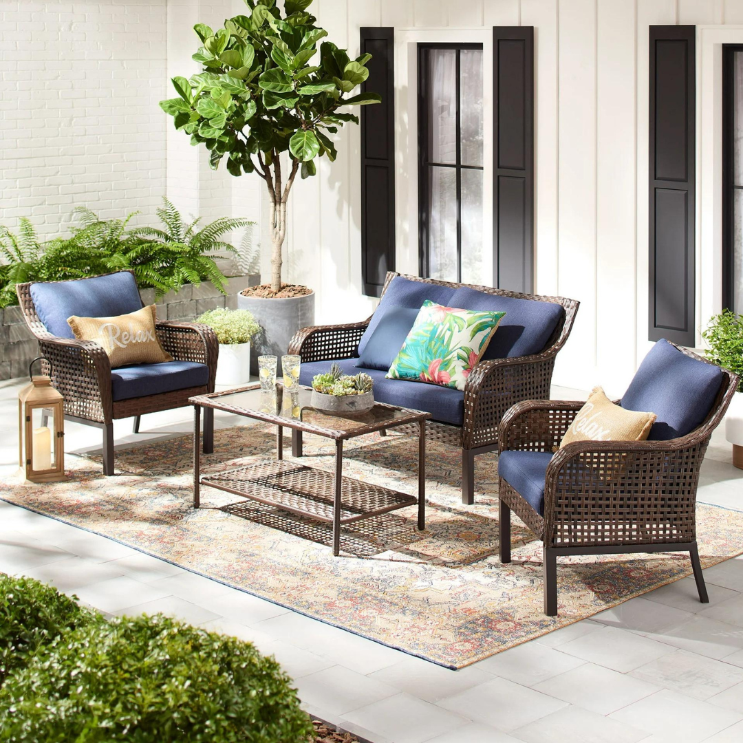 A wicker outdoor furniture set with two chairs, a sofa, and a coffee table, all with navy blue cushions, on a patterned area rug.