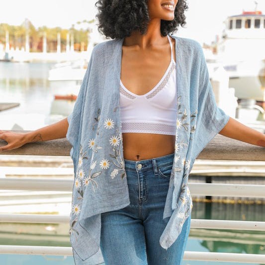 A woman wearing a white crop top, blue jeans, and a light blue cardigan with daisy patterns.