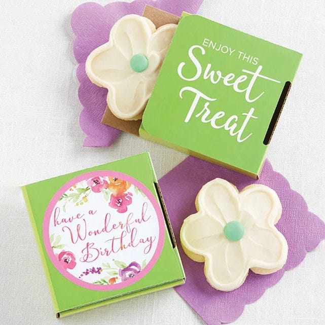 Two flower-shaped cookies with white icing and a green center, presented in green boxes with messages: \“Enjoy This Sweet Treat\“ and \“have a Wonderful Birthday\“ with floral designs.