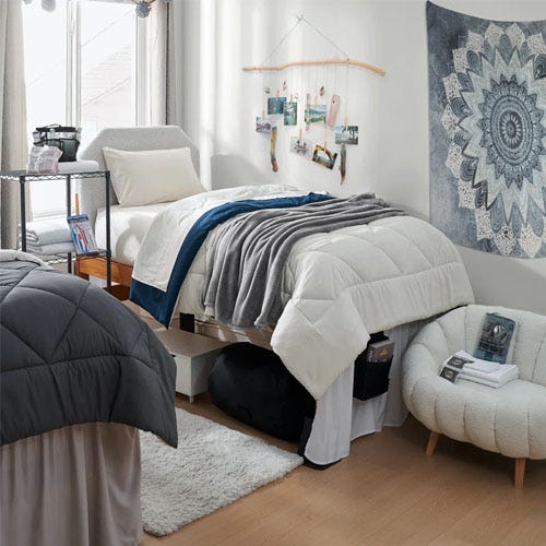 A bedroom setting with a bed featuring white and blue bedding, a nightstand, a sofa, and decorative wall hangings.