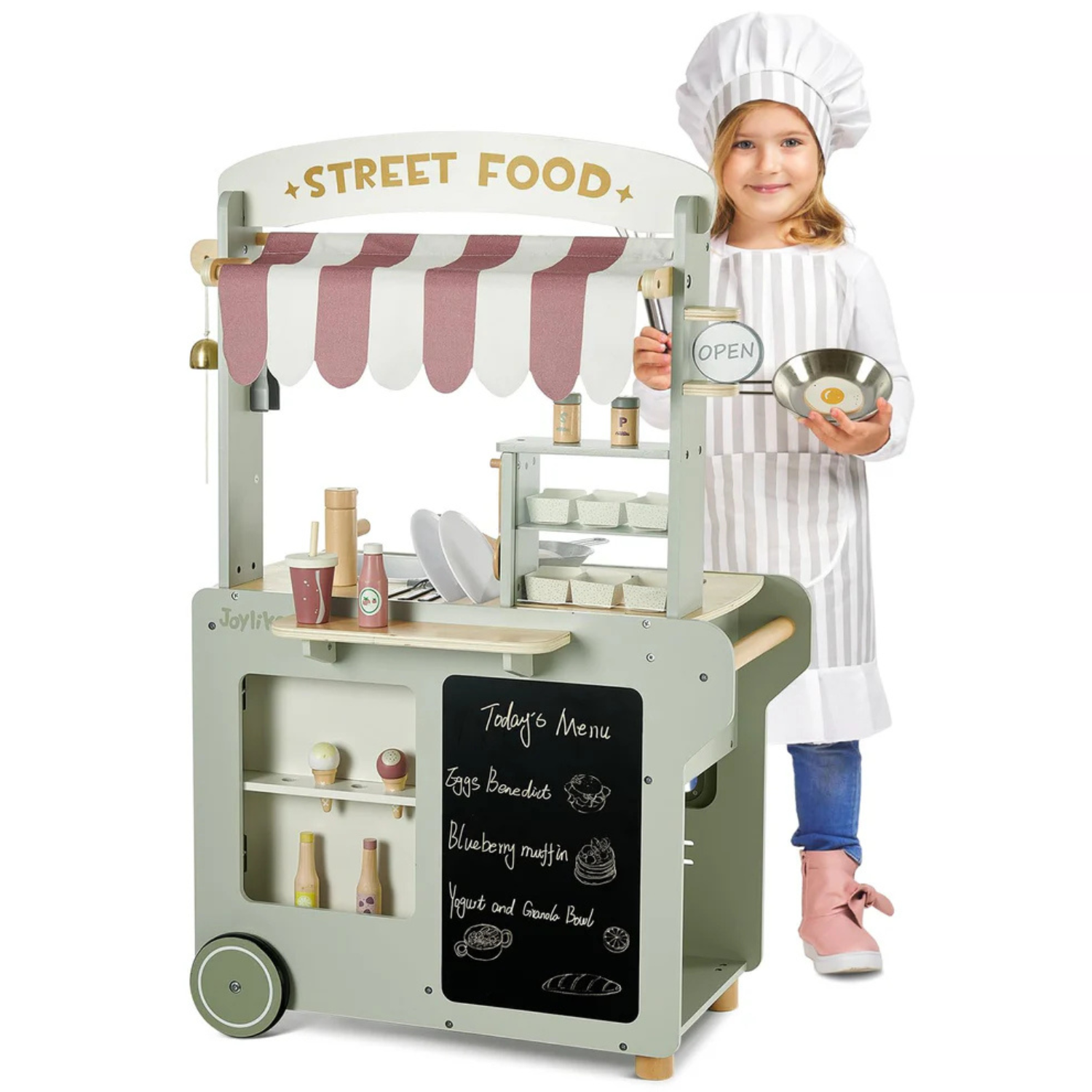 A kids' street food cart with a striped canopy features play items like condiments, cups, ice cream cones, and a chalkboard menu listing eggs benedict, blueberry muffin, and yogurt with granola. A child in a chef hat and apron stands beside it.