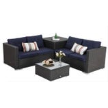 Outdoor wicker patio furniture set with navy cushions, includes a two-piece sofa with striped pillows, corner table, and a glass-top coffee table with a vase and decorative items.