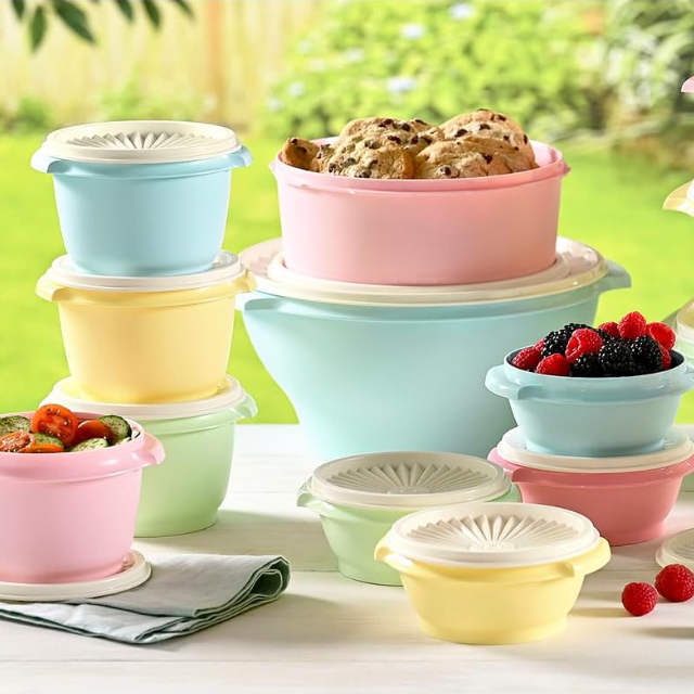 Assorted pastel-colored plastic bowls with lids, some filled with food such as berries and cookies.