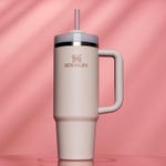 A beige Stanley tumbler with a lid and straw on a pink background.
