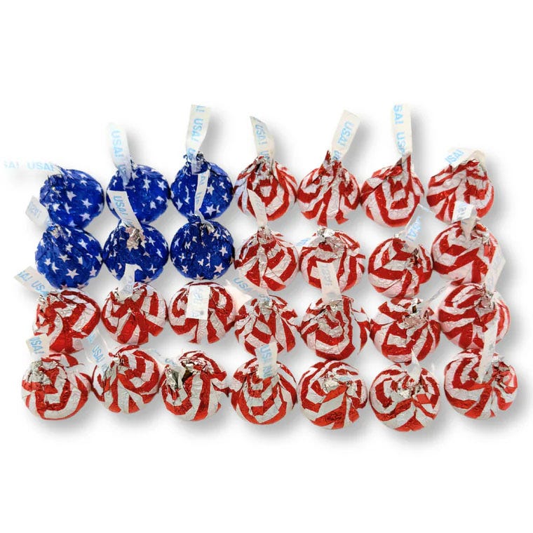 A collection of chocolate candies wrapped in American flag-themed foil, featuring blue with white stars and red with white stripes designs, each labeled with a \“USA\“ tag.