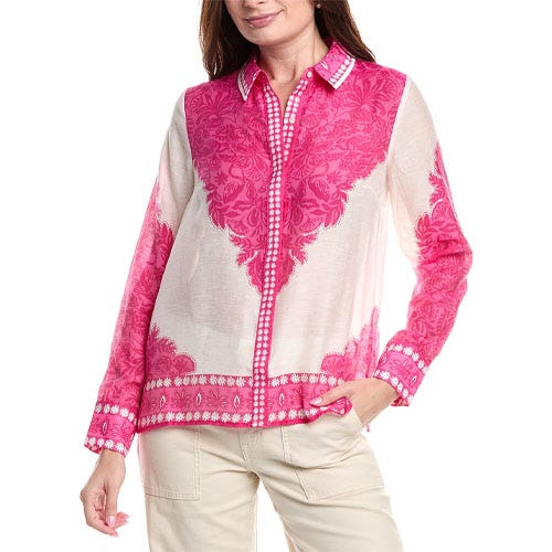 A woman is wearing a long-sleeve, pink and white button-up blouse with floral patterns, complemented by light-colored pants.