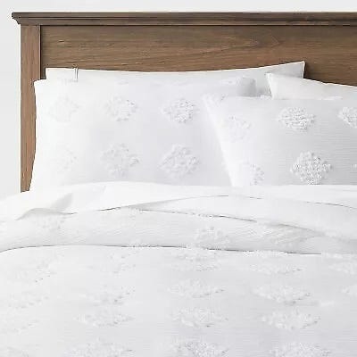 White embroidered bedding set on a bed with a wooden headboard, including pillowcases and a duvet cover.