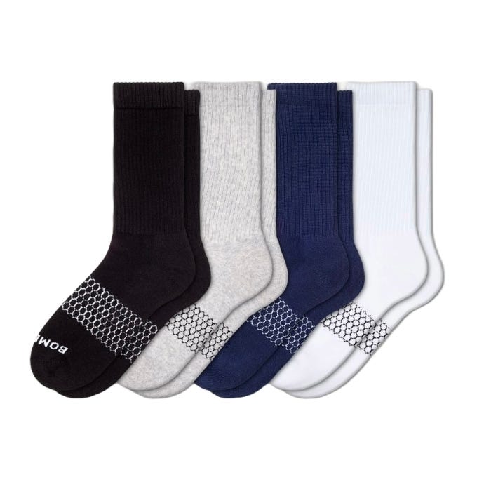 4-pack of Bombas men's calf socks in black, gray, navy, and white, featuring a honeycomb pattern at the arch for support and comfort.