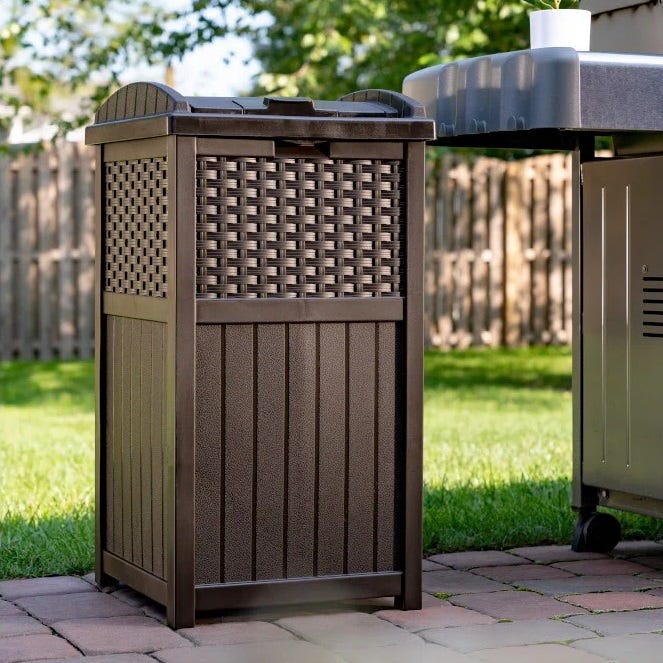 A brown outdoor trash can with a latticed design, next to a barbecue grill on a paved patio.