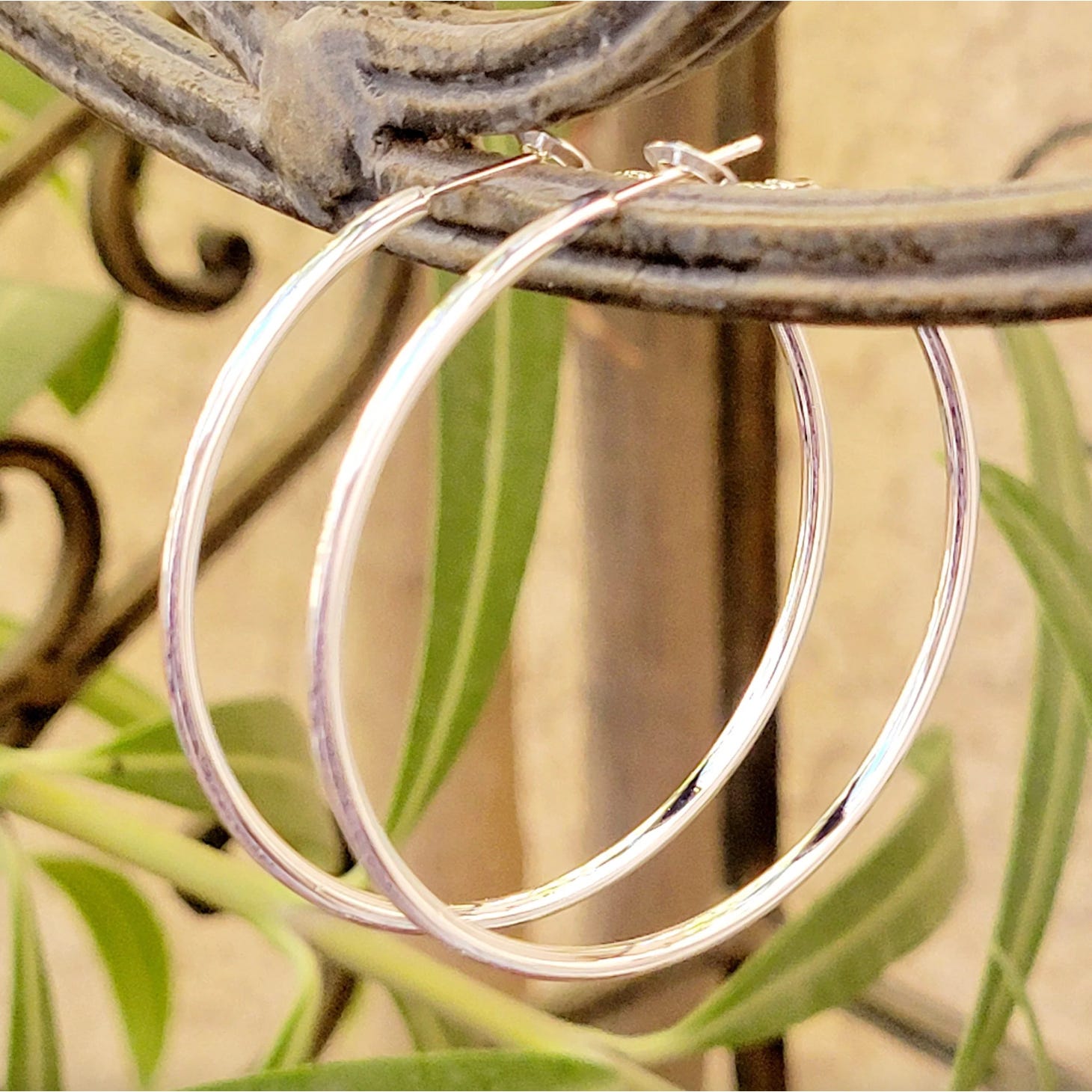 Sterling silver hoop earrings, 40mm in diameter, with a smooth, polished finish, are hanging on a decorative metal rack. They have a classic circular design.