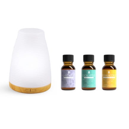 A white, cone-shaped aromatherapy diffuser with a wooden base is displayed alongside three small bottles of essential oils labeled as lavender, eucalyptus, and lemongrass.