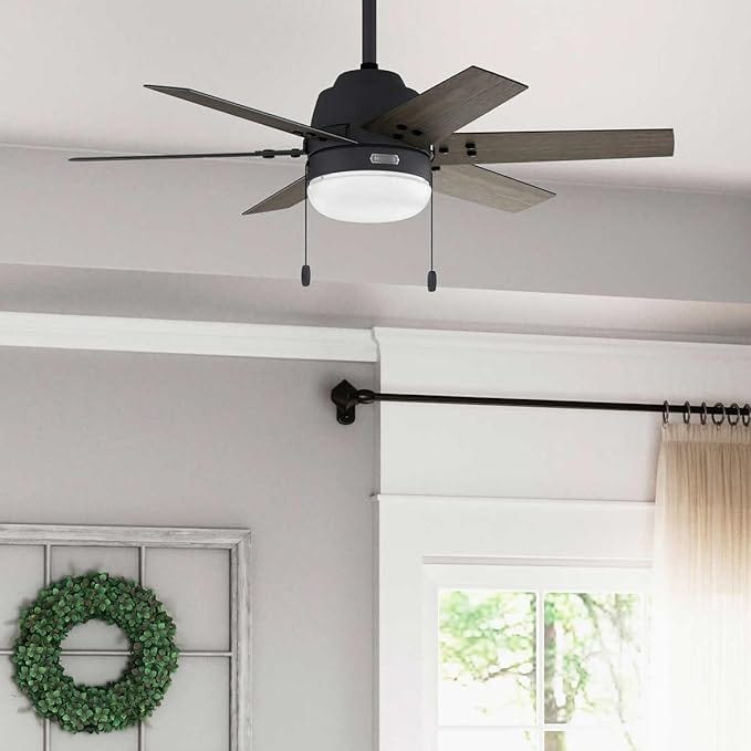 A ceiling fan with a light fixture, wooden blades, and a green wreath on a wall.