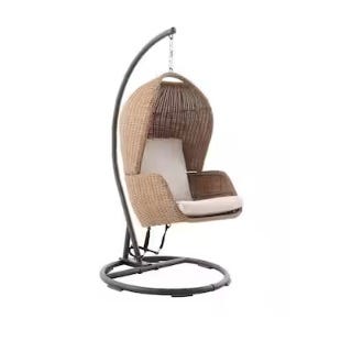 A hanging egg chair with a stand, featuring a wicker design and cushioned seating.
