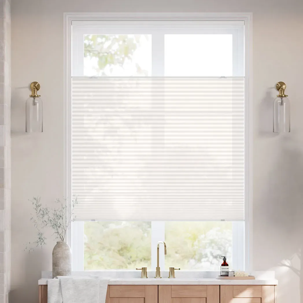 The photo features a modern bathroom with a window fitted with light-filtering blinds. The setup includes gold fixtures, two wall-mounted glass sconces, and a countertop with a vase and soap dispenser.