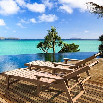 Two wooden sun loungers on a deck overlooking a tropical sea view.