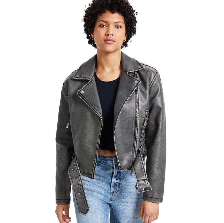 A person wearing a black biker jacket with silver zippers and a belted waist, paired with a black top and blue jeans.