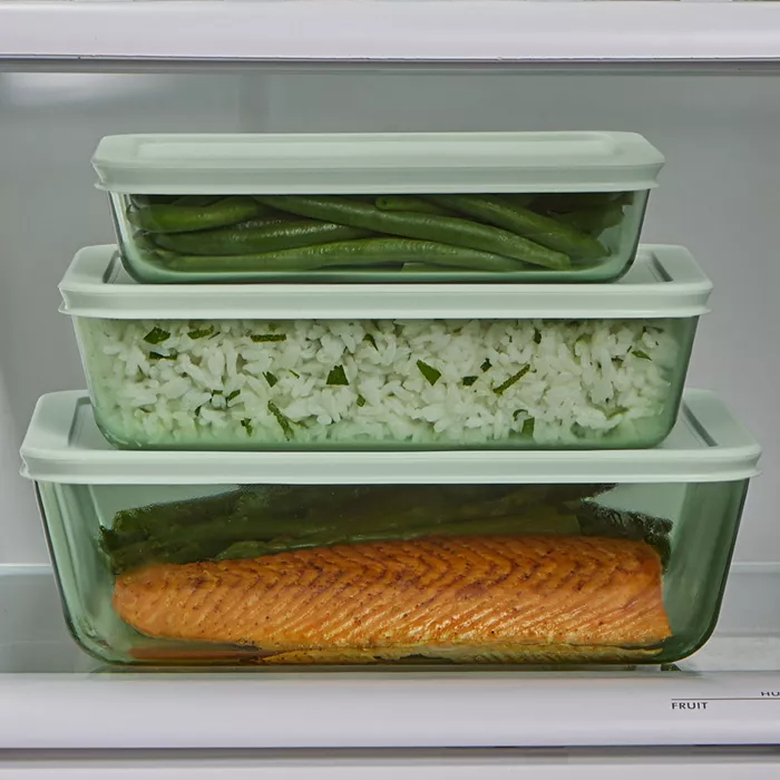 Three glass food containers with green beans, rice with herbs, and cooked salmon.