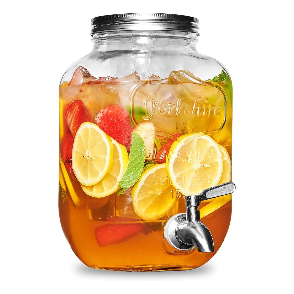 A clear beverage dispenser filled with iced tea and slices of lemon, strawberry, and mint leaves.
