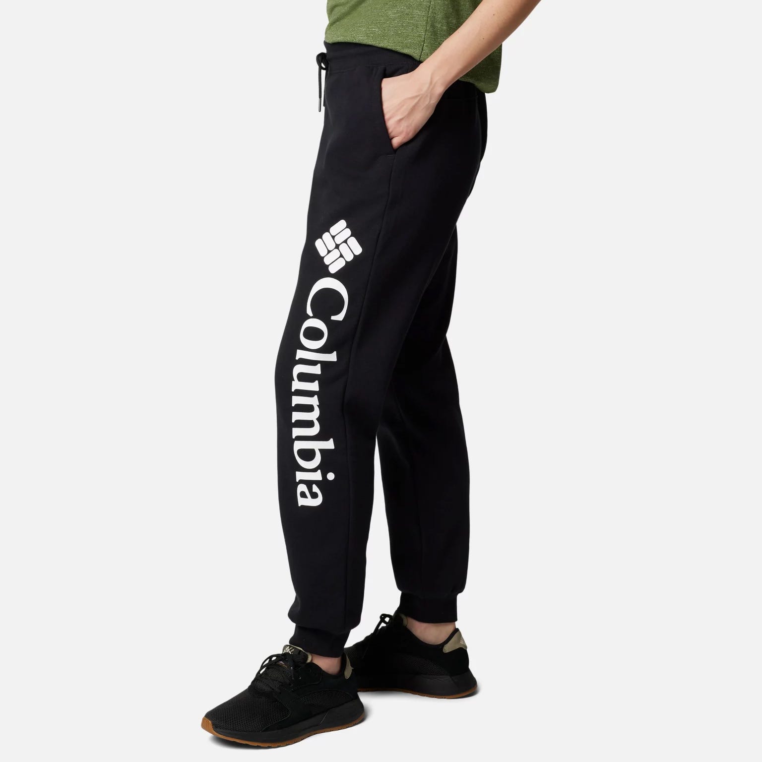A person is wearing dark pants with the Columbia brand logo on the left leg and black sneakers.