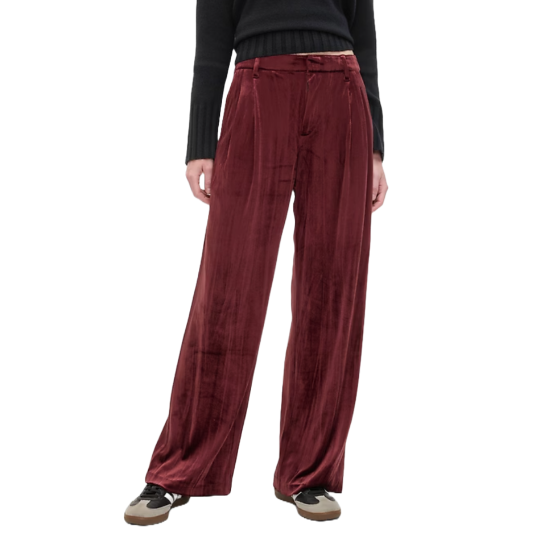 High-waisted, wide-leg, crinkle velvet trousers in a rich burgundy color, featuring pleats and a zip closure, paired with a black sweater and sneakers.