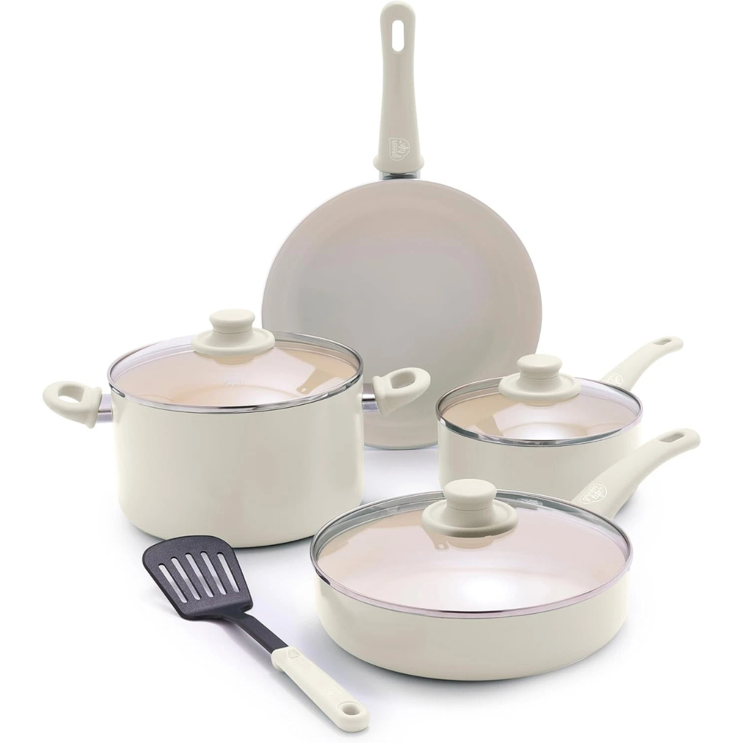A cream-colored cookware set featuring a frying pan, a small saucepan with a lid, a large pot with a lid, a deep sauté pan with a lid, and a black spatula.