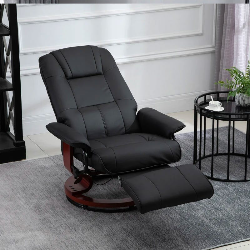 Black leather recliner chair with a separate matching footrest on a wooden base, placed in a room with a side table and plant.
