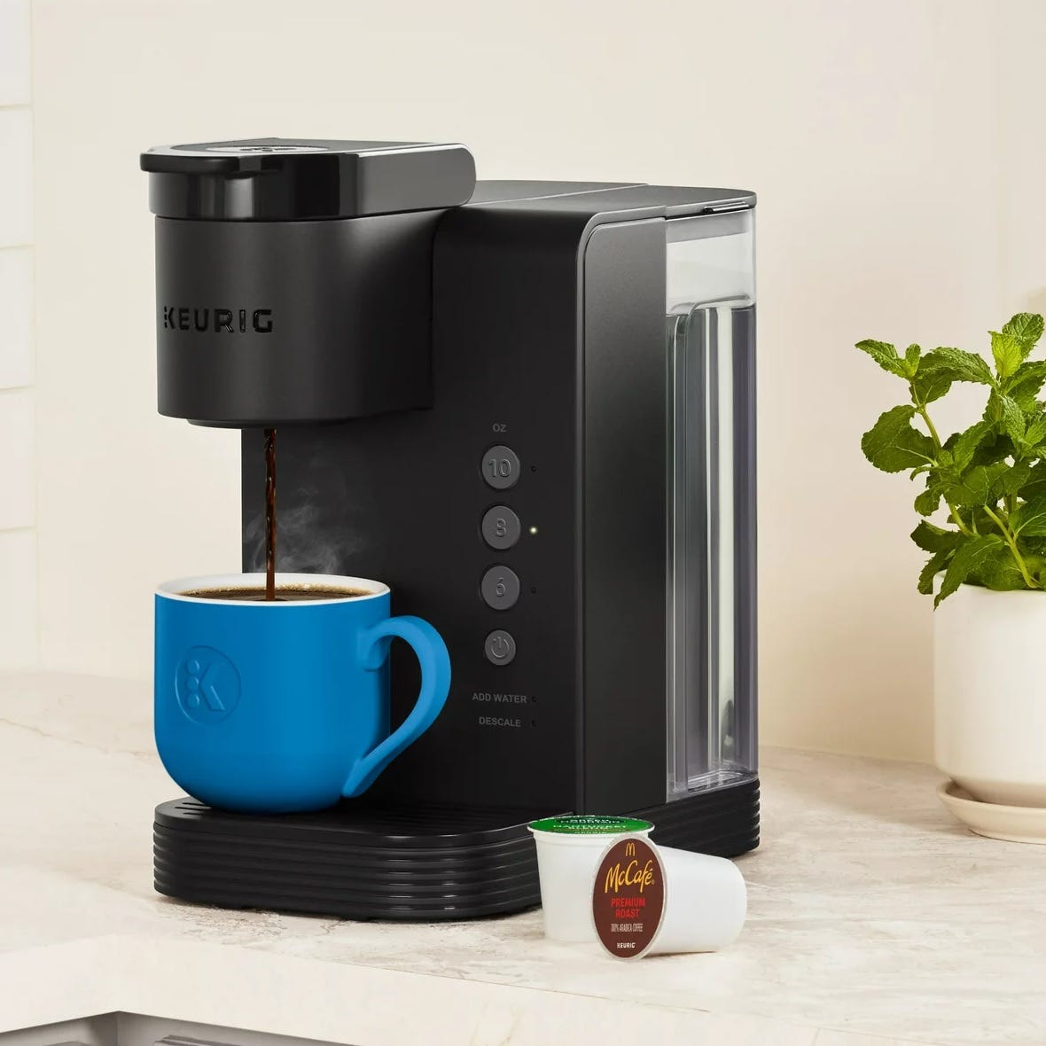 A Keurig coffee maker dispensing coffee into a blue mug alongside a McCafé K-Cup pod.