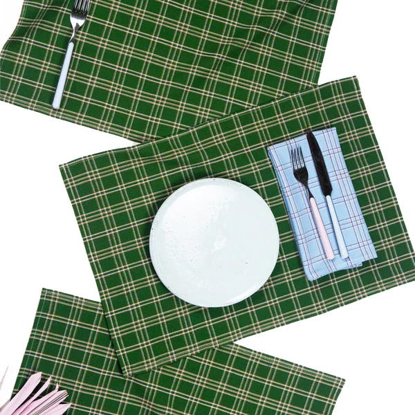 Four green and black plaid placemats are displayed with coordinating cutlery and a white plate on one, suggesting a table setting.
