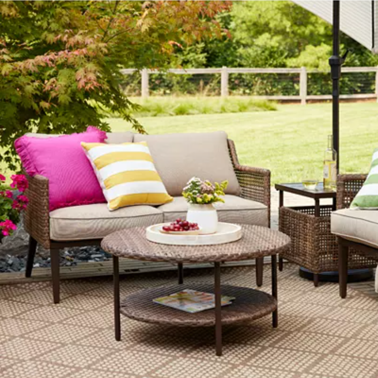 Outdoor wicker sofa with cushions, a round wicker coffee table, and colorful throw pillows.