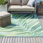 Outdoor furniture set on a deck with a colorful leaf-patterned rug, a two-seater sofa, and a woven side table.