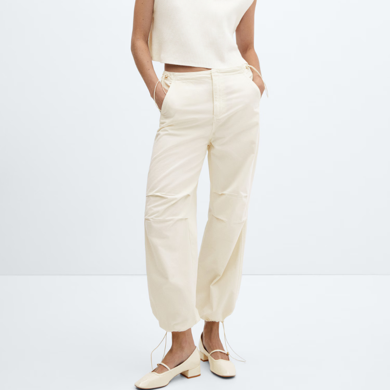 Cream-colored parachute pants with cargo pocket details and drawstring hems, paired with a white sleeveless top and cream flats.