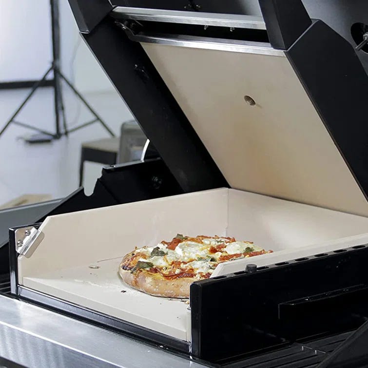 A pizza being placed inside a compact, countertop pizza oven.