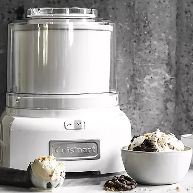 A Cuisinart Ice Cream Maker sits on a countertop next to two bowls of ice cream with toppings.