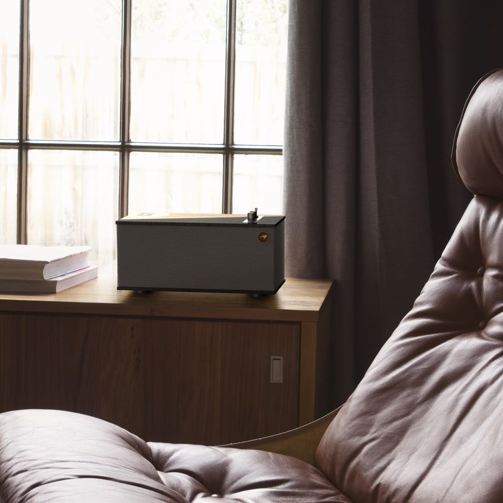 A modern turntable on a wooden cabinet beside a pile of books, with a leather armchair in the foreground.