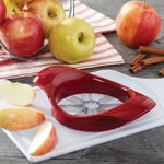 A red apple slicer on a white tray surrounded by whole apples and sliced apple pieces.