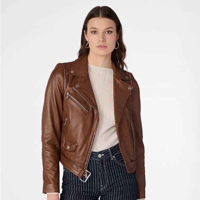A woman wearing a brown leather biker jacket over a white sweater and striped pants.