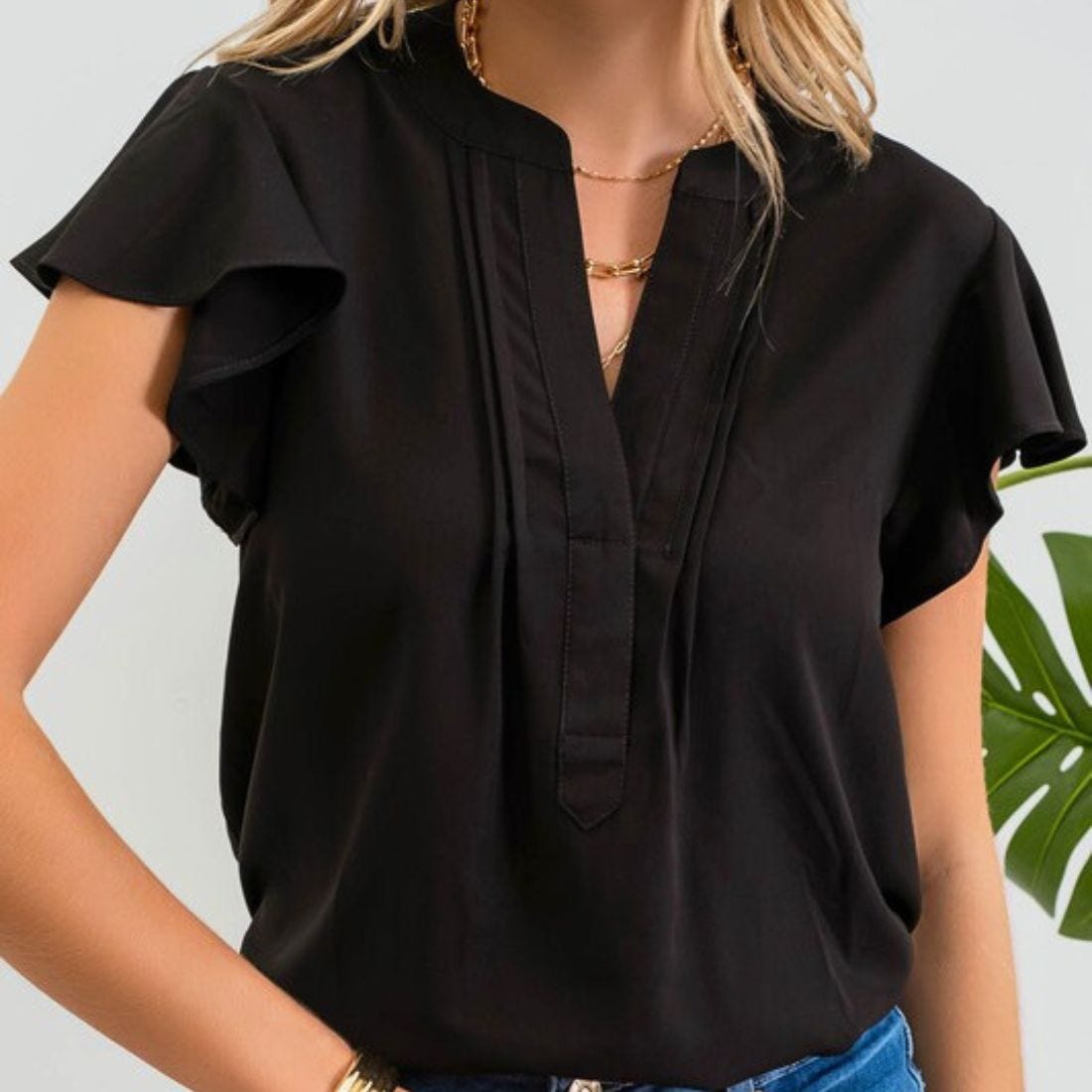 A woman wearing a black V-neck blouse with short flutter sleeves and layered necklaces.